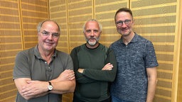 Helmut Gote, Uwe Schulz und Heiko Antoniewicz vor gelbem Hintergrund im WDR 5 Studio bei guter Laune.