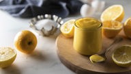 Symbolfoto eines Glas Lemon Curd auf einem Holzbrett – kann vom Rezept abweichen