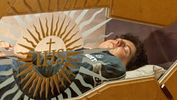 Das Bild zeigt den Leichnam des jungen Carlo Acutis der in einem gläsernen Sarg in der Kirche Santa Maria Maggiore in Assisi aufgebahrt ist  