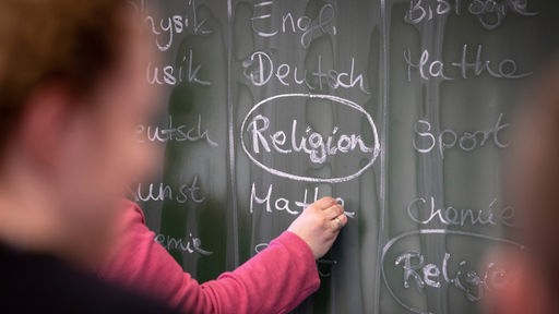 Auf einer Schultafel ist ein Stundenplan angeschrieben, das Wort Religion ist umkreist