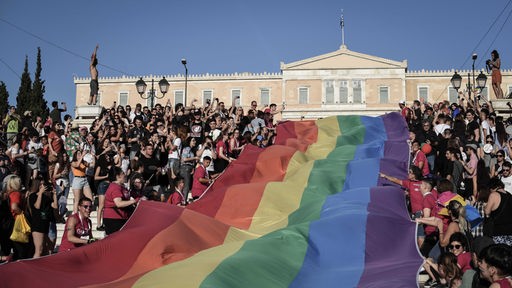 Feiernde Menschen entrollen bei der Pride Parade 2018 eine große Regenbogenflagge vor dem griechischen Parlament in Athen 