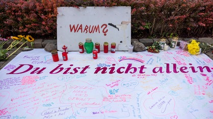 Nach der Messerattacke auf dem Solinger Stadtfest haben Menschen in der Nähe des Tatortes Nachrichten sowie Blumen und Kerzen hinterlassen. Es sind die Schriftzüge "Warum?" und "Du bist nicht allein" zu lesen (Foto vom 25.08.2024).