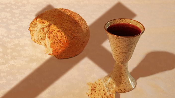 Elemente der Kommunion: Brot und Wein, darüber der Schatten eines Kreuz
