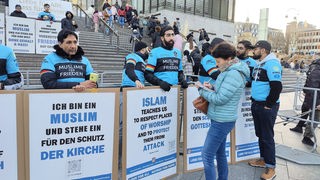 Mitglieder der Ahmadiyya-Gemeinde stehen mit Transparenten vor dem Kölner Dom