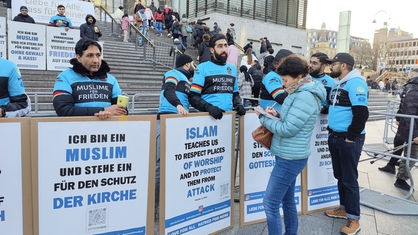 Mitglieder der Ahmadiyya-Gemeinde stehen mit Transparenten vor dem Kölner Dom