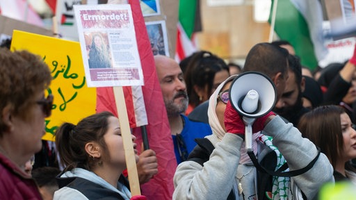 Menschen protestieren in Düsseldorf am 5. Oktober 2024 für einen Waffenstillstand im Nahostkonflikt. Eine junge Frau ruft in ein Megafon. 