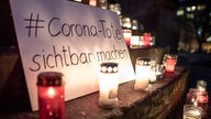 Kerzen und ein Schild mit der Aufschrift "Corona-Tote sichtbar machen" erinnern zu Jahresbeginn am Arnswalder Platz in Berlin an die im Zusammenhang mit dem Corona-Virus verstorbenen Menschen.