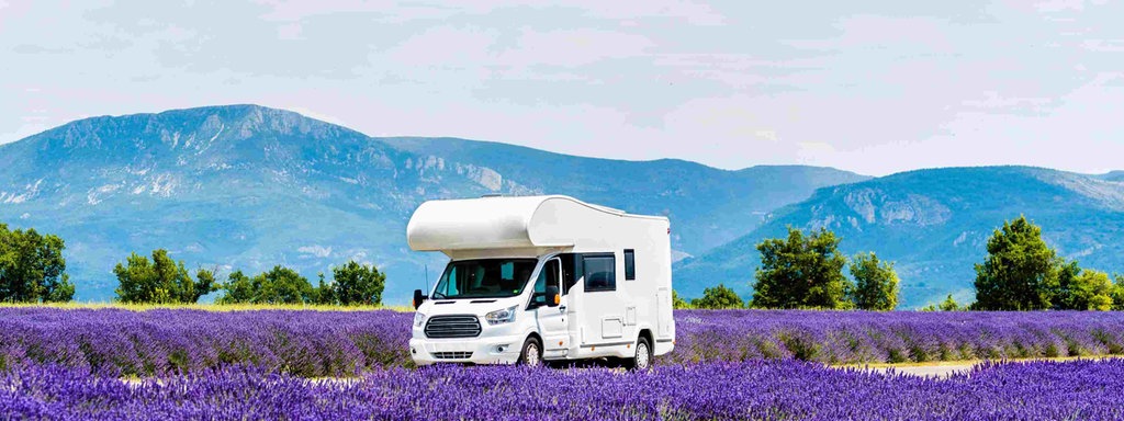 Beitragsbild zeigt einen Wohnwagen unterwegs in der Provence, Frankreich. Rechts und links der Straße sind Lavendelfelder. 