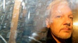 Das Beitragsbild des Dok5 "Collateral Fake?" zeigt Julian Assange auf dem Weg zum Gericht hinter der Fensterscheibe eines Autos 2019 in London.