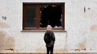 Das Beitragsbild des Dok5 Feature "Wasser bis zum Hals" zeigt eine junge Frau vor einer Hausfassade vor einem zerborstenen Fenster stehen. 