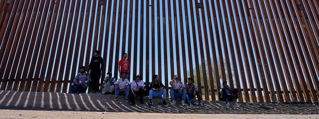 Das Beitragsbild des Dok5 "Auf Turnschuhen durch die Wüste" zeigt eine Gruppe Flüchtlinge im Schatten der amerikanischen Grenzmauer in der Region Tucson in 2023.