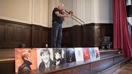 Eduard Meyer mit Posaune: Im Vordergrund stehen diverse, aufgereihte LPs seiner Schaffenszeit als Tontechniker, ua. von David Bowie.