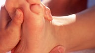 Symbolbild: Eine Masseurin führt eine Fußreflexzonen-Massage durch (Detail).