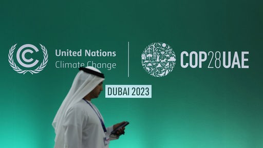 Ein Mann steht in Dubai vor einer Werbetafel zur Weltklimakonferenz COP28, 30.11.2023.