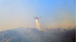 Ein Löschhubschrauber wirft Wasser ab, während ein Waldbrand auf dem Berg Parnitha in der Nähe von Athen, Griechenland, brennt, 29.06.2024. 