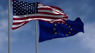 Flagen von USA und Europa wehen am sich verdunkeltem Himmel. 