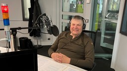 Bertram Dickerhof sitzt mit Kopfhörern vor einem Mikrofon in einem Studio des WDR und lächelt freundlich in die Kamera