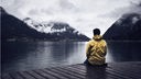 Ein Mann in einer gelben Jacke sitzt auf einem Holzsteg und blickt auf einen Bergsee