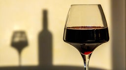 Ein Rotweinglas, im Hintergrund Schatten des Glases und einer Flasche