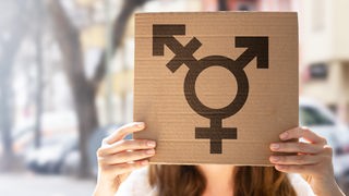 Eine Frau hält ein Schild mit dem Transgender-Symbol.