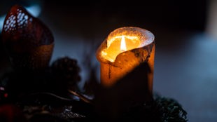 Eine einzelne Kerze auf einem Adventskranz in einem dunklen Zimmer