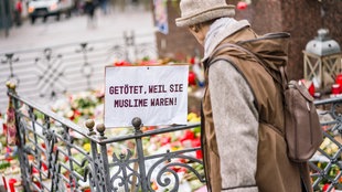 Eine Frau steht im Februar 2020 auf dem Marktplatz von Hanau, wo die Bürger mit Blumen, Plakaten und Kerzen ihre Trauer zum Ausdruck bringen. Auf einem Schild steht: "Getötet, weil sie Muslime waren!"