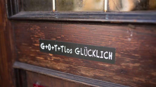  Ein Aufkleber mit der Aufschrift "Gottlos Glücklich" klebt an einer hölzernen Haustüre.