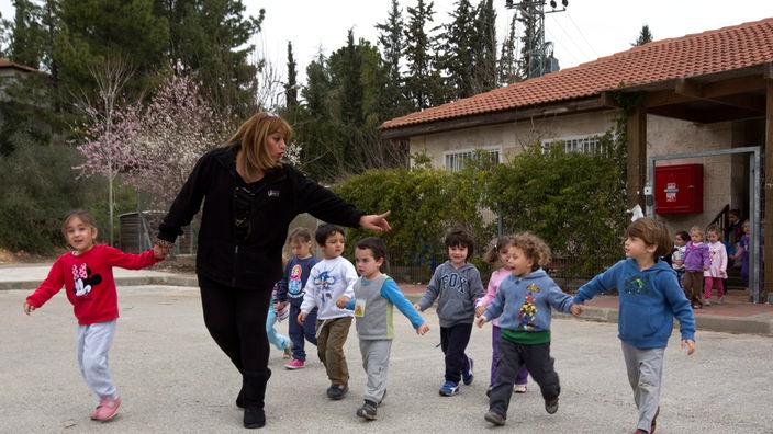 Kinder auf einem Hof,geleitet von einer Kindergärtnerin.