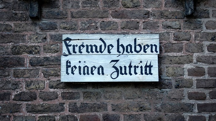 Auf einem Hof hängt an einer Backsteinwand ein Schild mit der Aufschrift "Fremde haben keinen Zutritt".