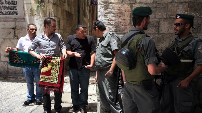 Israelische Sicherheitskräfte diskutieren mit Palästinensern mit Gebetsteppichen am Rande der Jerusalemer Altstadt.