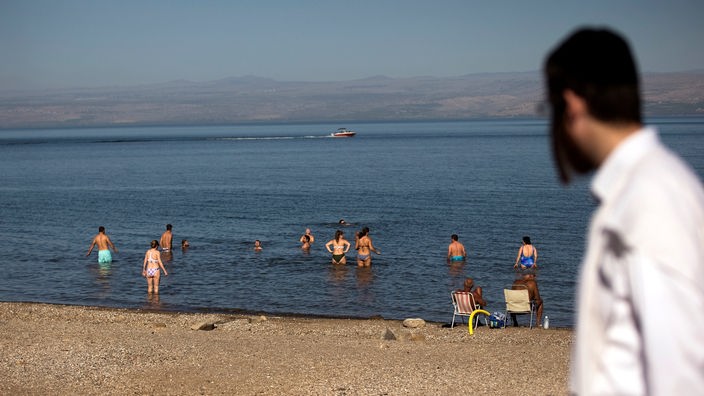 Ein Mann mit Kippa und Bart blickt auf badende Menschen im See Genezareth.