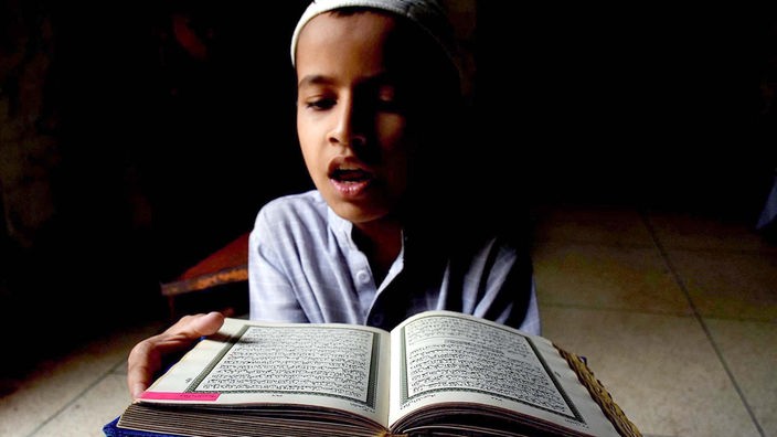 Ein Junge rezitiert aus einem aufgeschlagenen Koran.