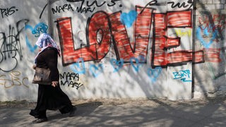 Eine Muslima mit Kopftuch läuft an einem Grafitti vorbei, das den Schriftzug "LOVE" schreibt.