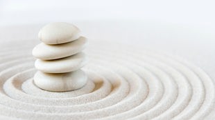 Symbolfoto für Zen-Meditation: Geharkter Sand und aufeinander ruhende weiße Steine