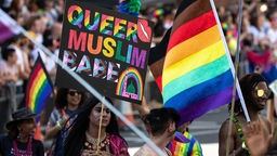 Ein Teilnehmer einer Gay Pride Parade hält ein Schild mit der regenbogenfarbenen Aufschrift: "Queer Muslim Babe"