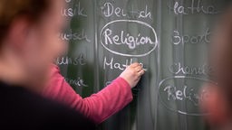 Auf einer Schultafel steht das Wort Religion.