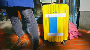 Das Bild zeigt die Beine der Frau und ihren gelben Rollkoffer, der mit einer ukrainischen Fahne beklebt ist, am Hamburger Hbf im März 2022
