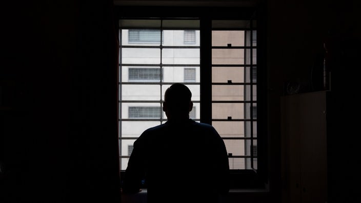 Ein Insasse einer Justizvollzugsanstalt (JVA) steht in seiner Einzelzelle im Gegenlicht am Fenster.