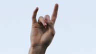 Eine hand formt den "Teufelsgruß" (auch mano cornuta, italienisch "gehörnte Hand"): Der Zeigefinger und der kleine Finger werden von der Handfläche abgespreitzt, während der Daumen, Mittel- und Ringfinger eine Faust bilden.