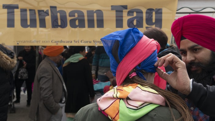 Ein Mitglied der Sikh-Gemeinde bindet einer Passantin auf dem Potsdamer Platz in Berlin einen Turban. Dort hatten Sikhs zum Turban-Tag geladen um Interessierten die Bedeutung der Kopfbedeckung näher zu bringen.