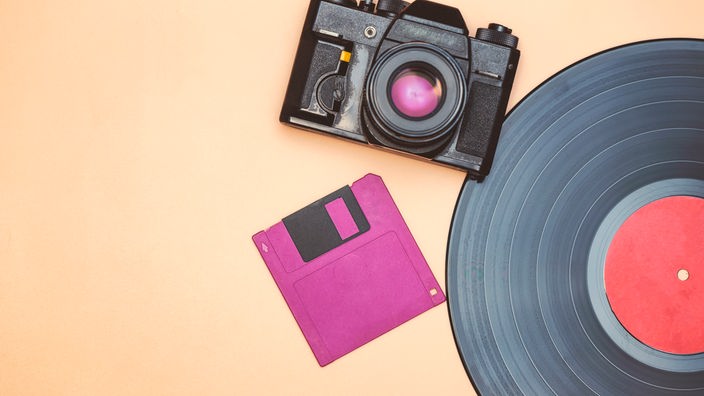 Eine Vinyl-Schallplatte, eine Diskette und eine analgoge Forokamera verweisen auf den rapiden Wandel im technonogischen Bereich.