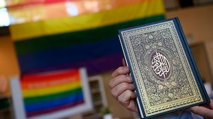 Ein Imam hält bei der Vorstellung der Anlaufstelle Islam und Diversity (AID) der Ibn Rushd-Goethe Moschee einen Koran vor eine Regenbogenflagge.