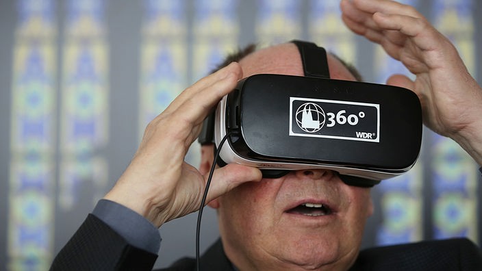 Der Domprobst des Kölner Doms, Gerd Bachner, blickt erstaunt durch eine VR-Brille im Rahmen eines Virtual Reality Projekts des WDR.