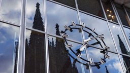 Auf der gläsernen Fassade des Hauptbahnhofs-Gebäudes spiegelt sich hinter der Bahnhofs-Uhr die Silhouette des Kölner Doms.