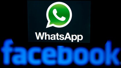 Illustration - Das Logo des Kurznachrichten-Dienstes WhatsApp ist auf einem Smartphone zu sehen, welches vor das Logo des weltgrößten sozialen Online-Netzwerkes Facebook gehalten wird