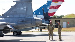 Zwei Soldaten stehen auf dem Flugplatz vor zwei Kampfjets