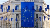 Sarajevo: Eine riesige Flagge der Europäischen Union hängt an einem Gebäude, während kleinere Flaggen eine Hauptstraße schmücken