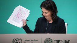 Annalena Baerbock hält auf einer Pressekonferenz im Rahmen der COP28 Papiere hoch