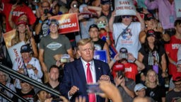 Donald Trump steht bei einer Rally zwischen Unterstützern mit Fahnen und Plakaten