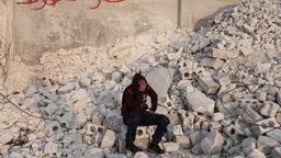 15-Jähriger in Kapuzenpuillover sitzt auf Trümmern und stützt den Kopf in der Hand